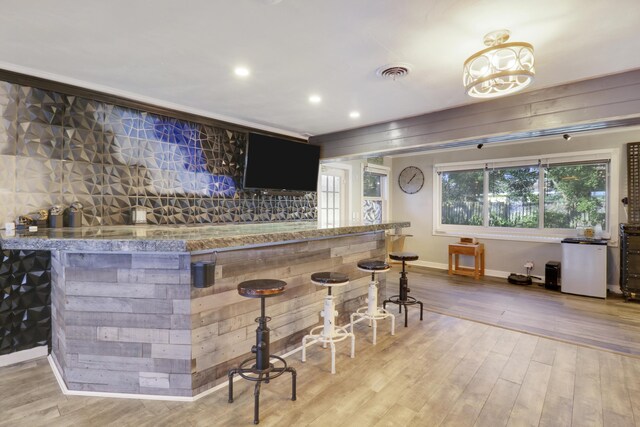 bar with light hardwood / wood-style flooring, ornamental molding, ceiling fan, and stone counters