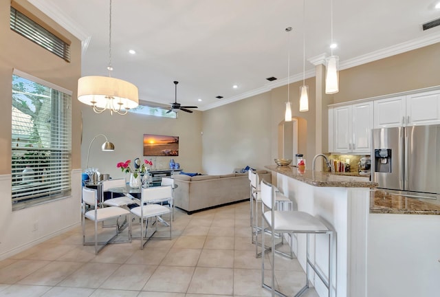 kitchen featuring stainless steel fridge with ice dispenser, hanging light fixtures, light stone countertops, ceiling fan with notable chandelier, and white cabinets