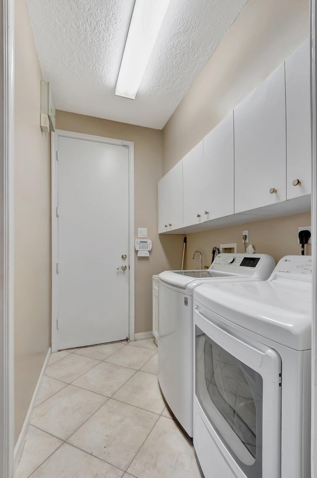 washroom with washing machine and dryer, cabinets, light tile patterned flooring, and a textured ceiling