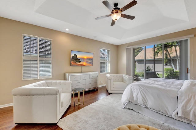 bedroom with ceiling fan, dark hardwood / wood-style floors, a tray ceiling, and multiple windows