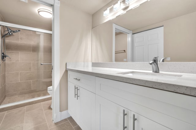 bathroom with tiled shower, vanity, tile patterned flooring, and toilet