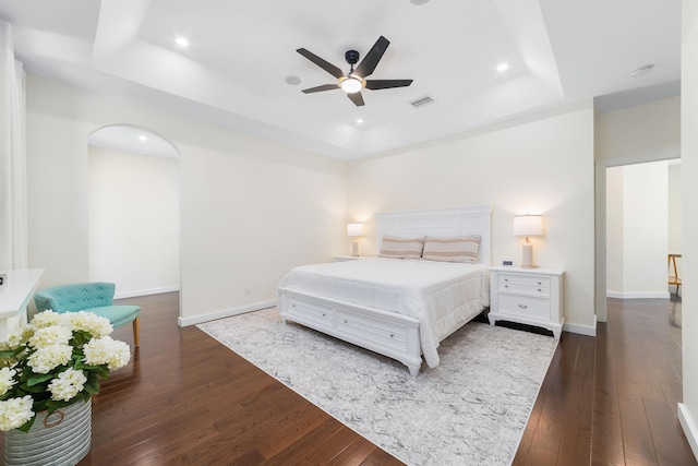 bedroom with ceiling fan, dark hardwood / wood-style flooring, and a tray ceiling