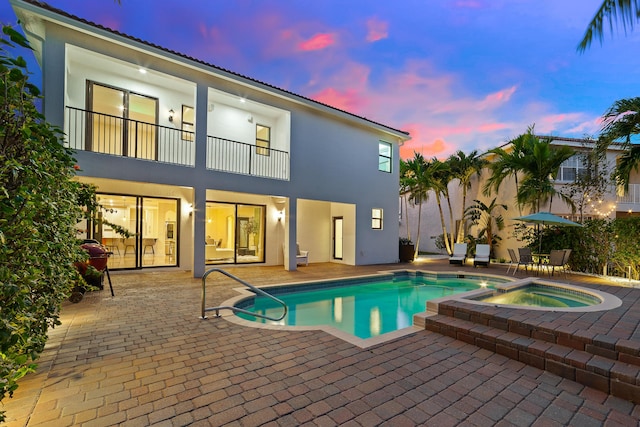 pool at dusk with an in ground hot tub and a patio