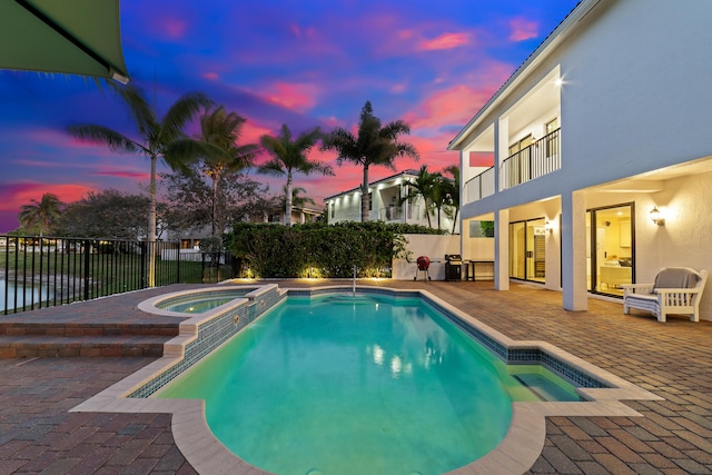 pool at dusk featuring an in ground hot tub and a patio