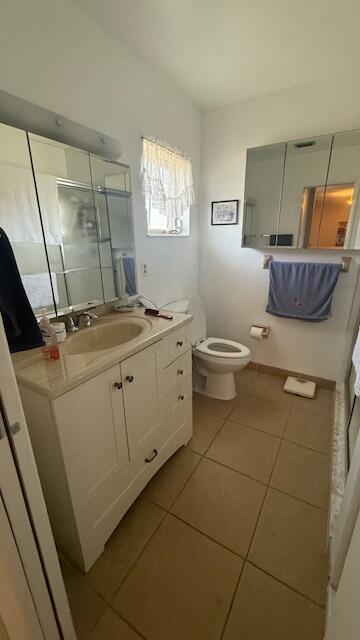 bathroom featuring tile patterned flooring, vanity, toilet, and a shower with door