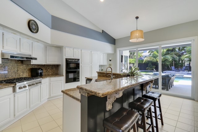 kitchen with hanging light fixtures, range hood, vaulted ceiling, decorative backsplash, and a center island with sink