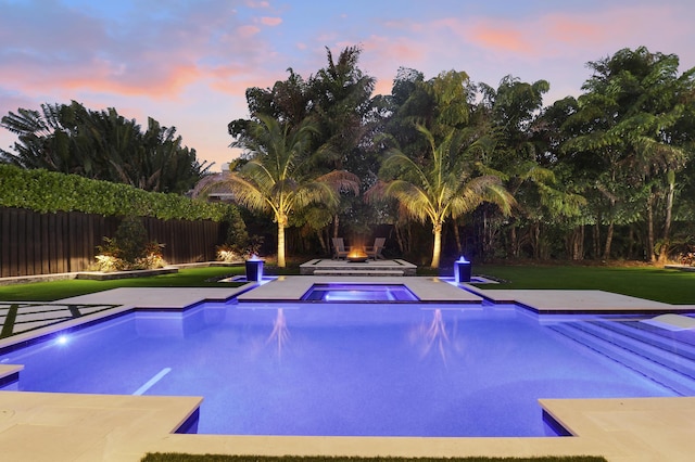 pool at dusk featuring a lawn and an in ground hot tub