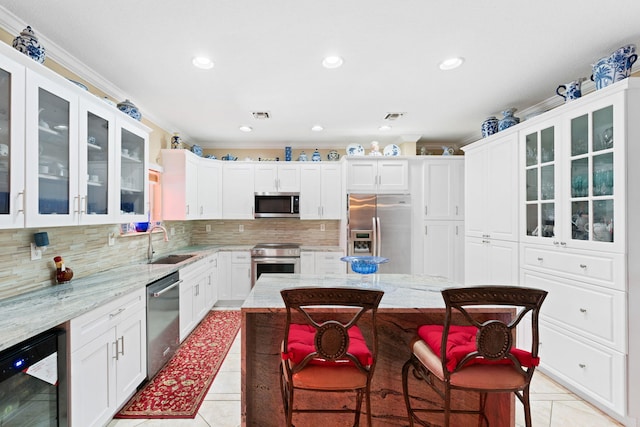 kitchen with appliances with stainless steel finishes, a kitchen breakfast bar, light stone counters, beverage cooler, and a center island