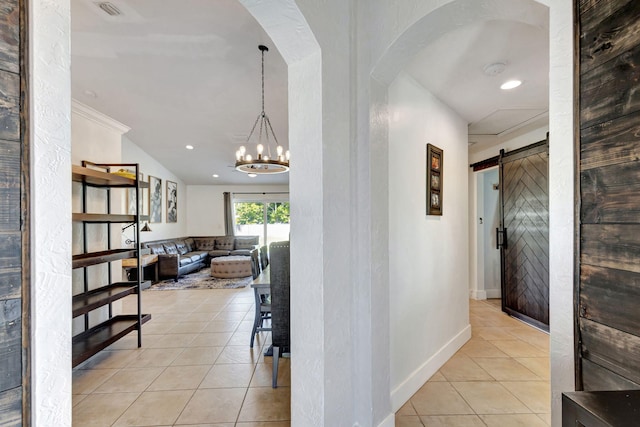 corridor with a barn door, crown molding, light tile patterned flooring, and an inviting chandelier