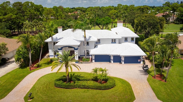 view of front facade featuring an attached garage, a tile roof, a chimney, and decorative driveway