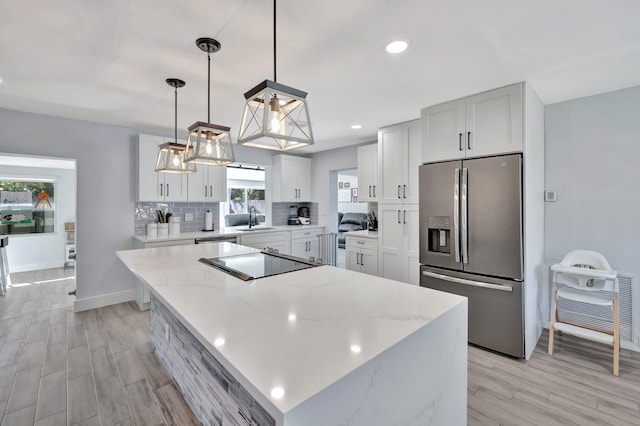 kitchen featuring pendant lighting, white cabinets, a kitchen island, light stone counters, and stainless steel appliances