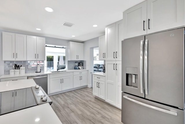 kitchen with light wood-type flooring, tasteful backsplash, stainless steel appliances, sink, and white cabinetry