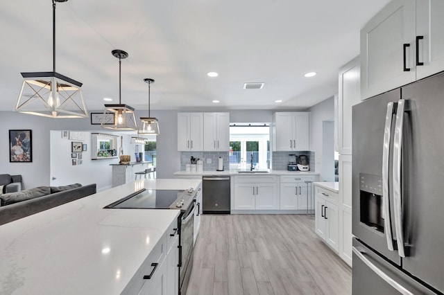 kitchen featuring hanging light fixtures, light stone countertops, appliances with stainless steel finishes, tasteful backsplash, and white cabinetry