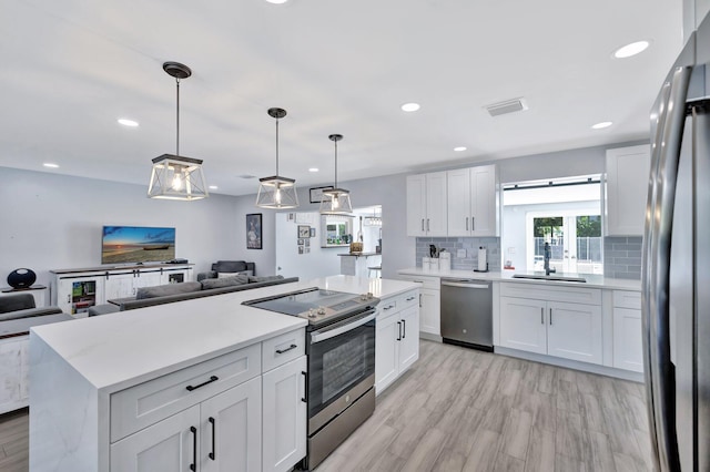 kitchen with white cabinetry, sink, stainless steel appliances, backsplash, and pendant lighting