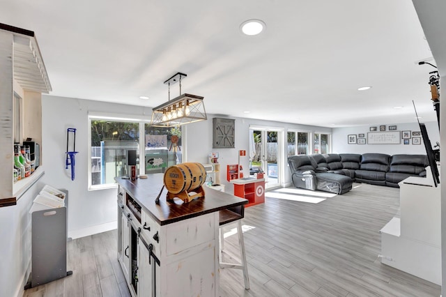 kitchen with white cabinetry, wooden counters, decorative light fixtures, a breakfast bar area, and light wood-type flooring