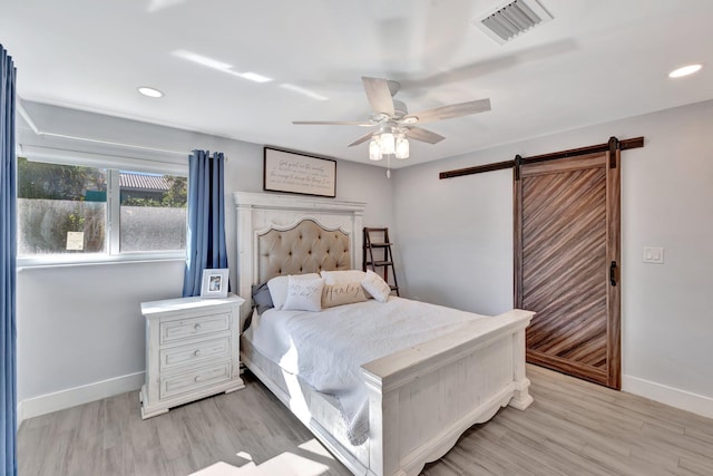 bedroom with ceiling fan, a barn door, and light wood-type flooring