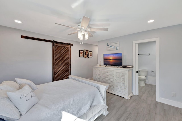 bedroom with a barn door, ceiling fan, light hardwood / wood-style flooring, and ensuite bath