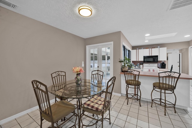 dining space featuring a skylight, french doors, light tile patterned floors, and a textured ceiling