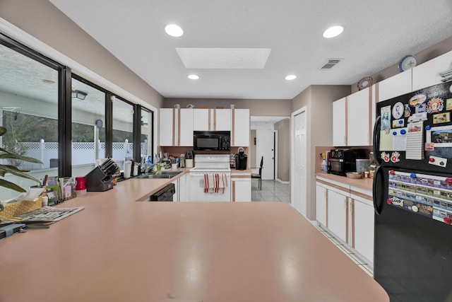 kitchen with black appliances, sink, a skylight, light tile patterned flooring, and white cabinetry