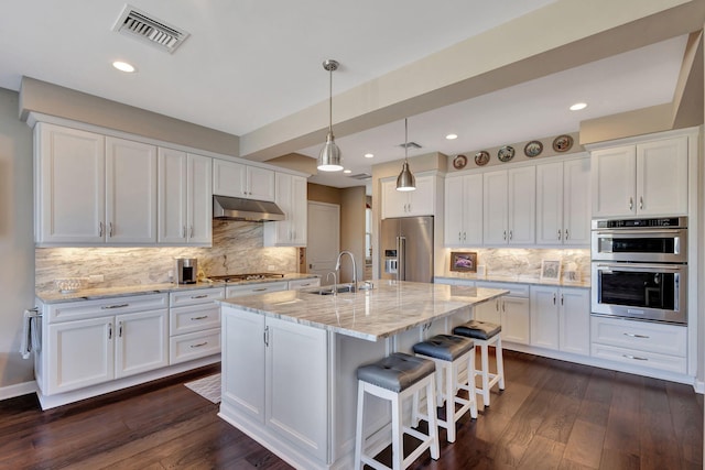 kitchen featuring light stone countertops, appliances with stainless steel finishes, a center island with sink, and white cabinets