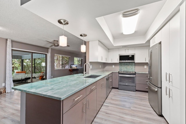 kitchen featuring sink, stainless steel appliances, a raised ceiling, kitchen peninsula, and white cabinets