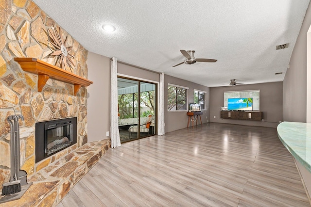 unfurnished living room with a stone fireplace, ceiling fan, a textured ceiling, and light wood-type flooring