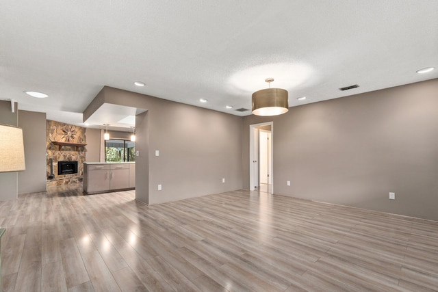 unfurnished living room with a fireplace, a textured ceiling, and light wood-type flooring