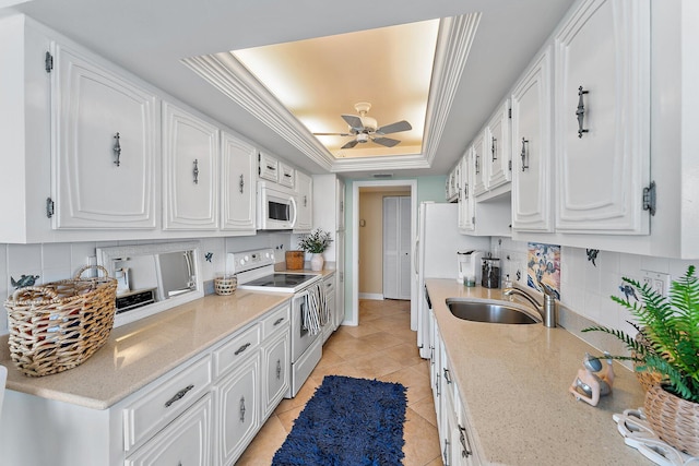 kitchen with sink, light tile patterned floors, a raised ceiling, white appliances, and white cabinets