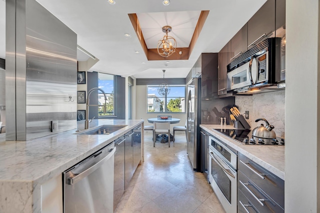 kitchen with light stone countertops, sink, stainless steel appliances, a chandelier, and a tray ceiling