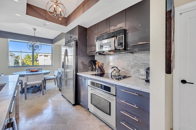 kitchen with a chandelier, appliances with stainless steel finishes, a tray ceiling, and decorative light fixtures