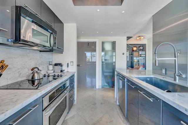 kitchen featuring black appliances, decorative backsplash, light stone counters, and sink