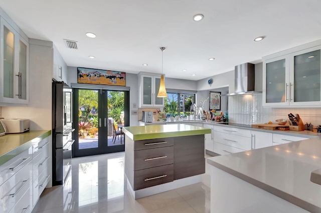 kitchen featuring hanging light fixtures, french doors, wall chimney exhaust hood, and white cabinetry