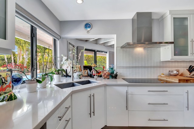 kitchen featuring black electric cooktop, sink, white cabinets, and wall chimney range hood