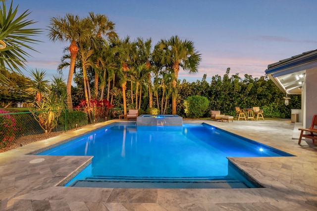 pool at dusk featuring an in ground hot tub and a patio