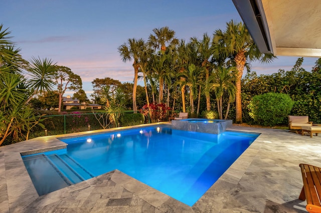 pool at dusk featuring an in ground hot tub and a patio