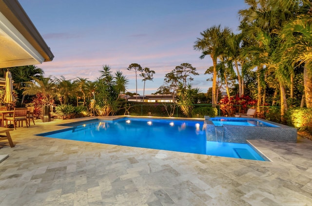 pool at dusk featuring an in ground hot tub and a patio