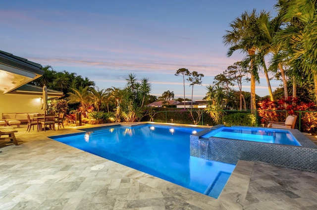 pool at dusk with an in ground hot tub and a patio