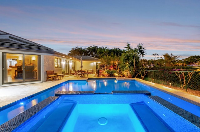 pool at dusk with a patio area and an in ground hot tub