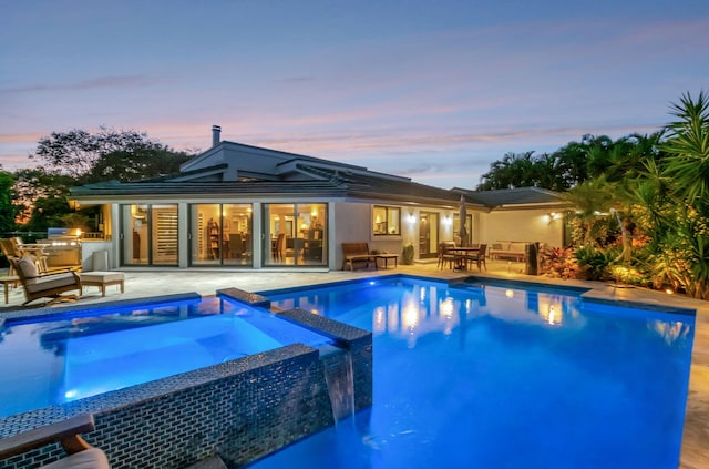 pool at dusk with an in ground hot tub and a patio