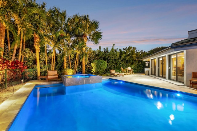 pool at dusk with a patio area and an in ground hot tub