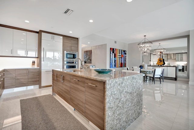 kitchen with stainless steel appliances, sink, decorative light fixtures, white cabinets, and a spacious island