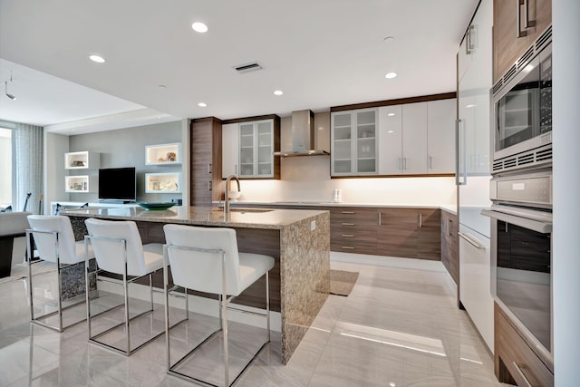 kitchen featuring light stone counters, wall chimney exhaust hood, stainless steel appliances, white cabinetry, and sink