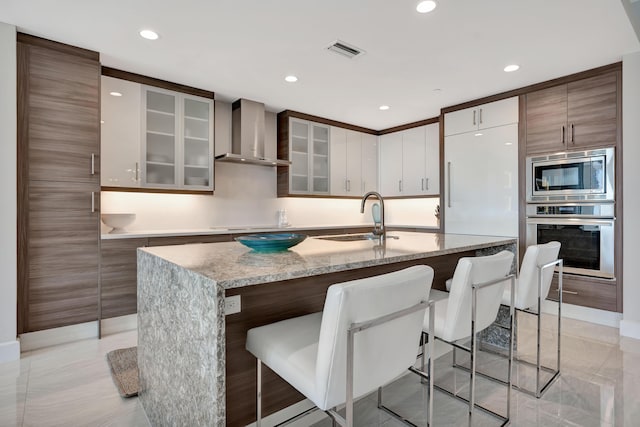 kitchen with appliances with stainless steel finishes, wall chimney range hood, a center island with sink, and sink