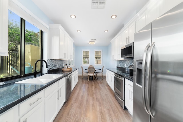 kitchen featuring dark stone countertops, stainless steel appliances, white cabinets, light hardwood / wood-style flooring, and sink