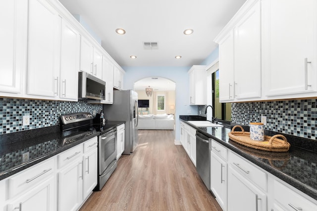 kitchen with appliances with stainless steel finishes, light hardwood / wood-style floors, dark stone counters, sink, and white cabinetry