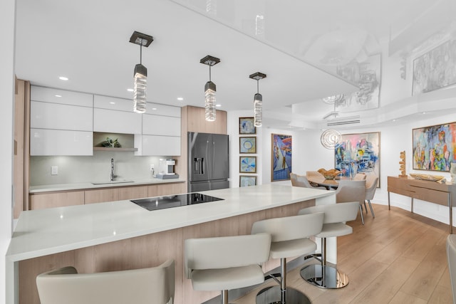 kitchen featuring stainless steel refrigerator with ice dispenser, black electric cooktop, sink, light hardwood / wood-style flooring, and white cabinetry