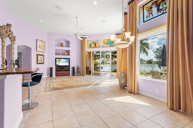 interior space featuring ceiling fan with notable chandelier, light tile patterned floors, and built in shelves