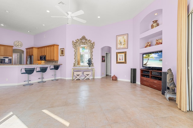 living room with light tile patterned flooring, ceiling fan, built in features, and a towering ceiling