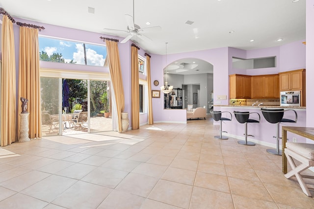 kitchen with light tile patterned flooring, a towering ceiling, a breakfast bar area, stainless steel oven, and kitchen peninsula