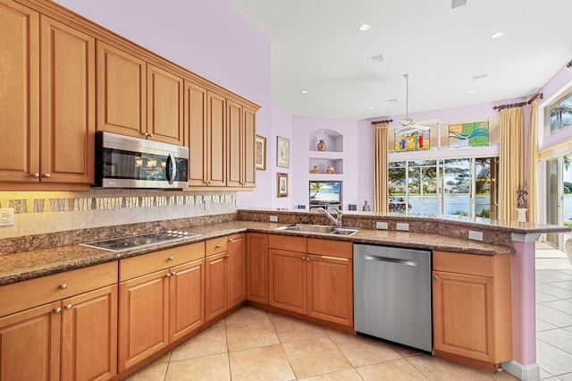 kitchen with appliances with stainless steel finishes, sink, dark stone counters, light tile patterned floors, and kitchen peninsula